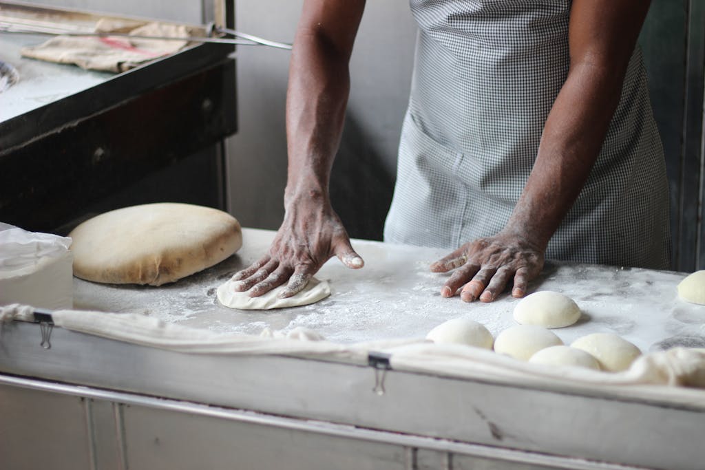 A baker in an indoor kitchen kneading dough for bread preparation, showcasing traditional baking techniques.